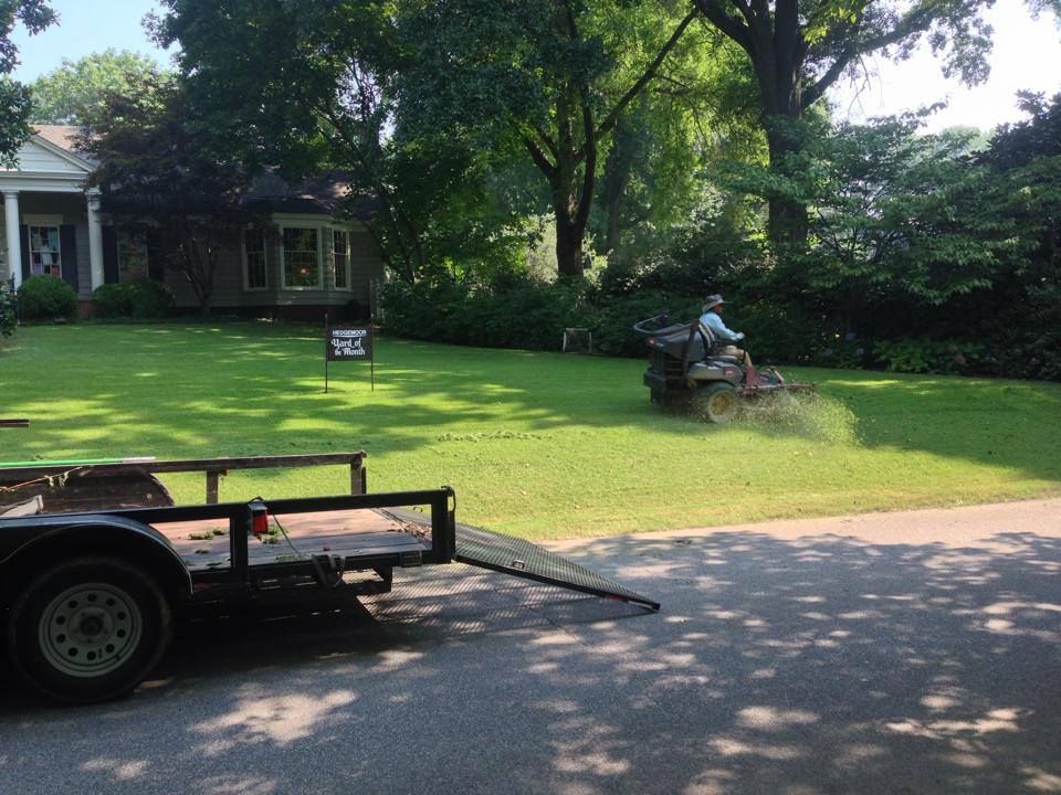 A lawn mower is being towed by a trailer in front of a house