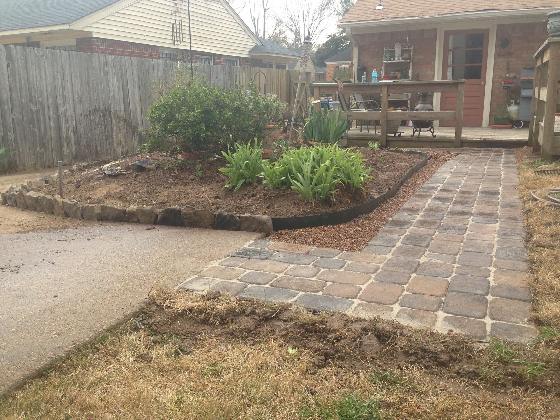 A brick walkway leading to a house with a fence in the background.