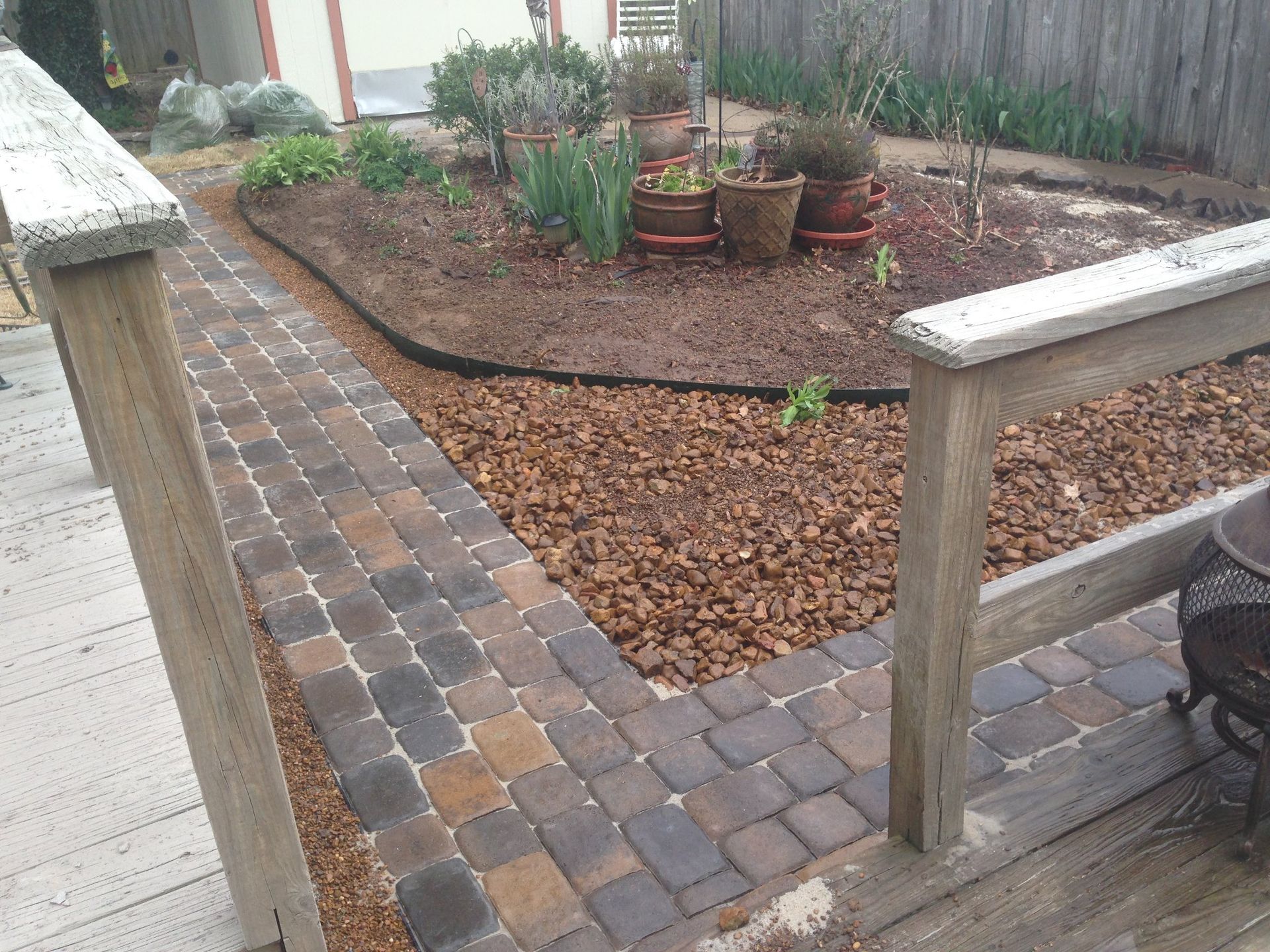 A brick walkway leading to a garden with potted plants and mulch.