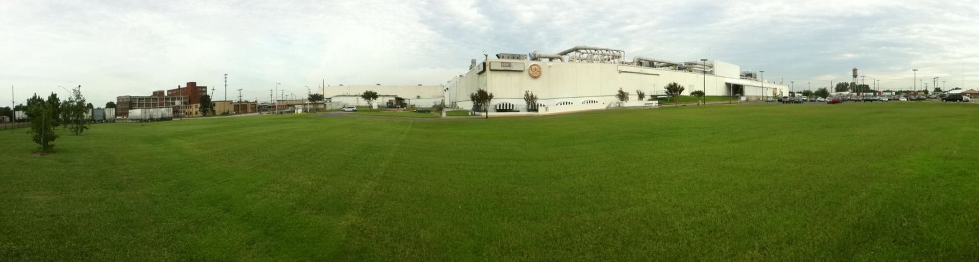 A large white building is sitting in the middle of a grassy field.