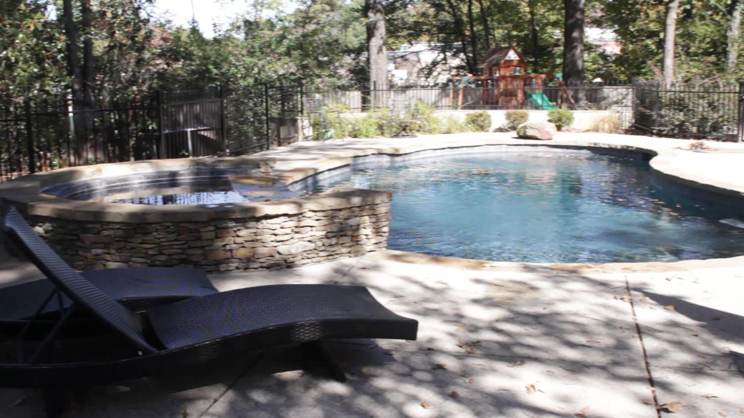 A large swimming pool with a hot tub in the backyard surrounded by trees.