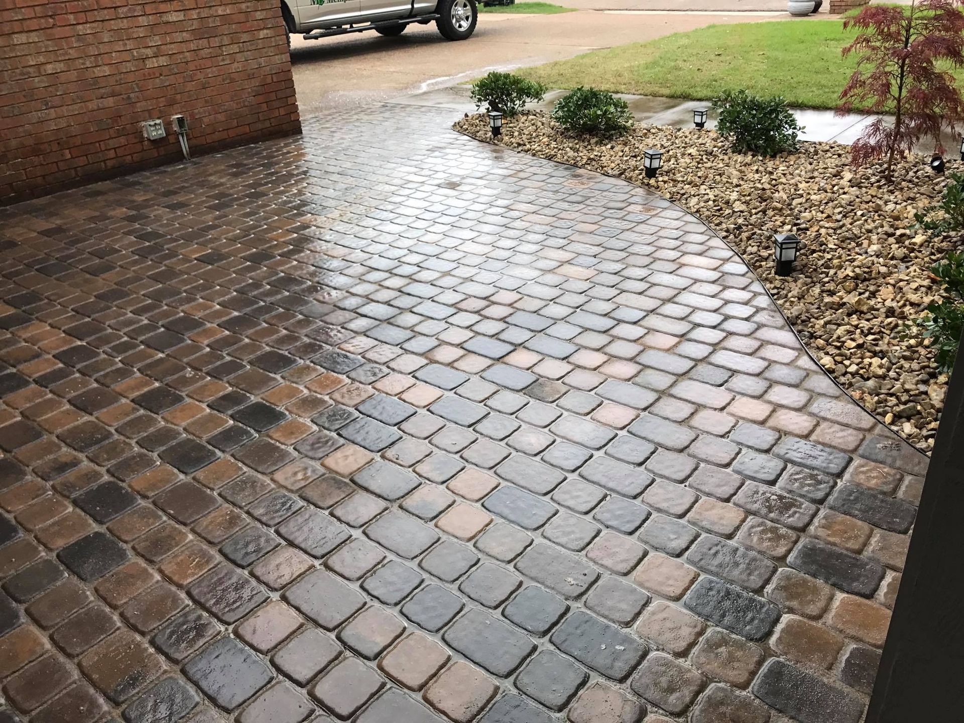 A brick walkway leading to a driveway with a truck parked in the background.
