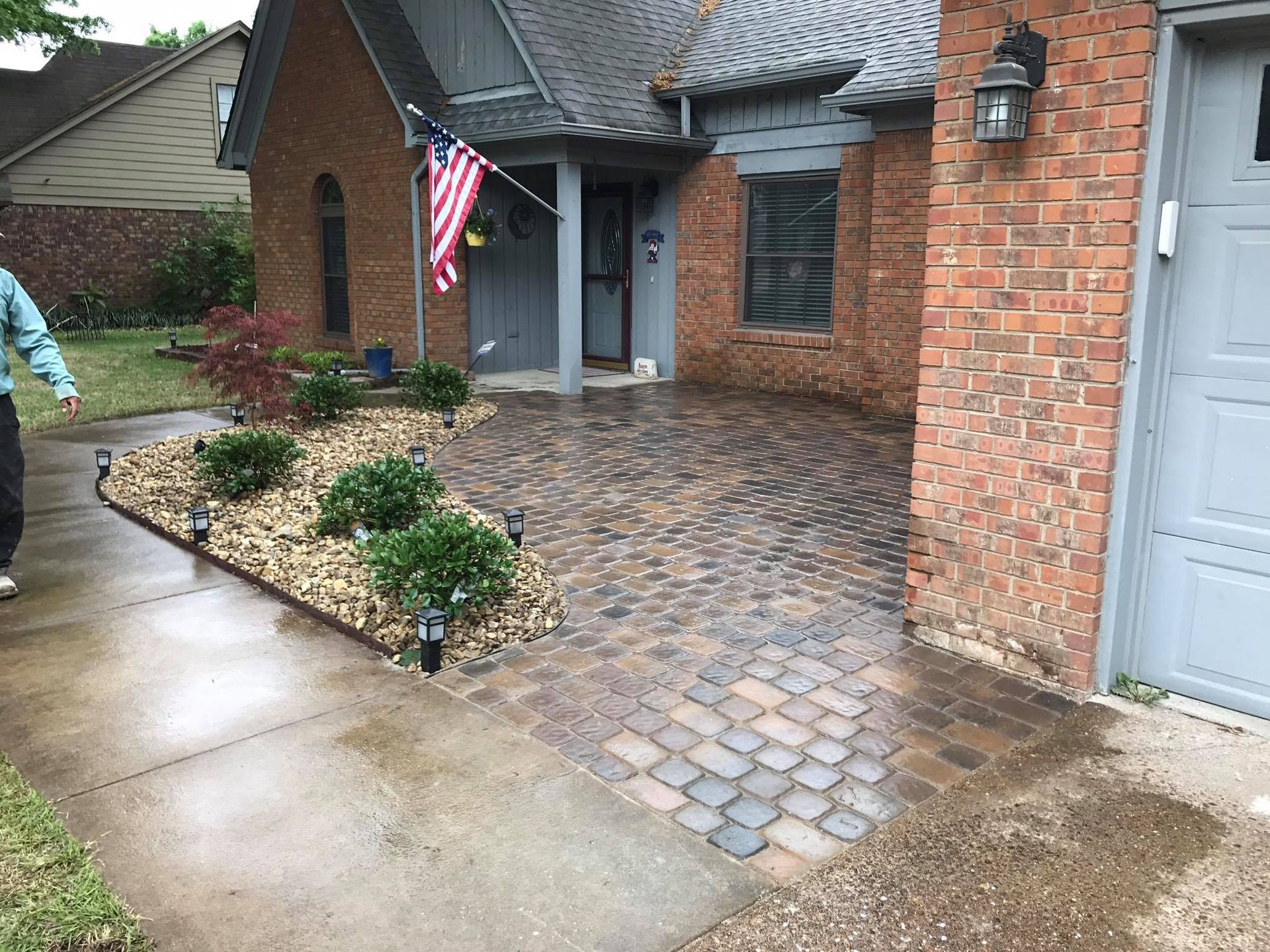 A man is walking down a sidewalk in front of a brick house.