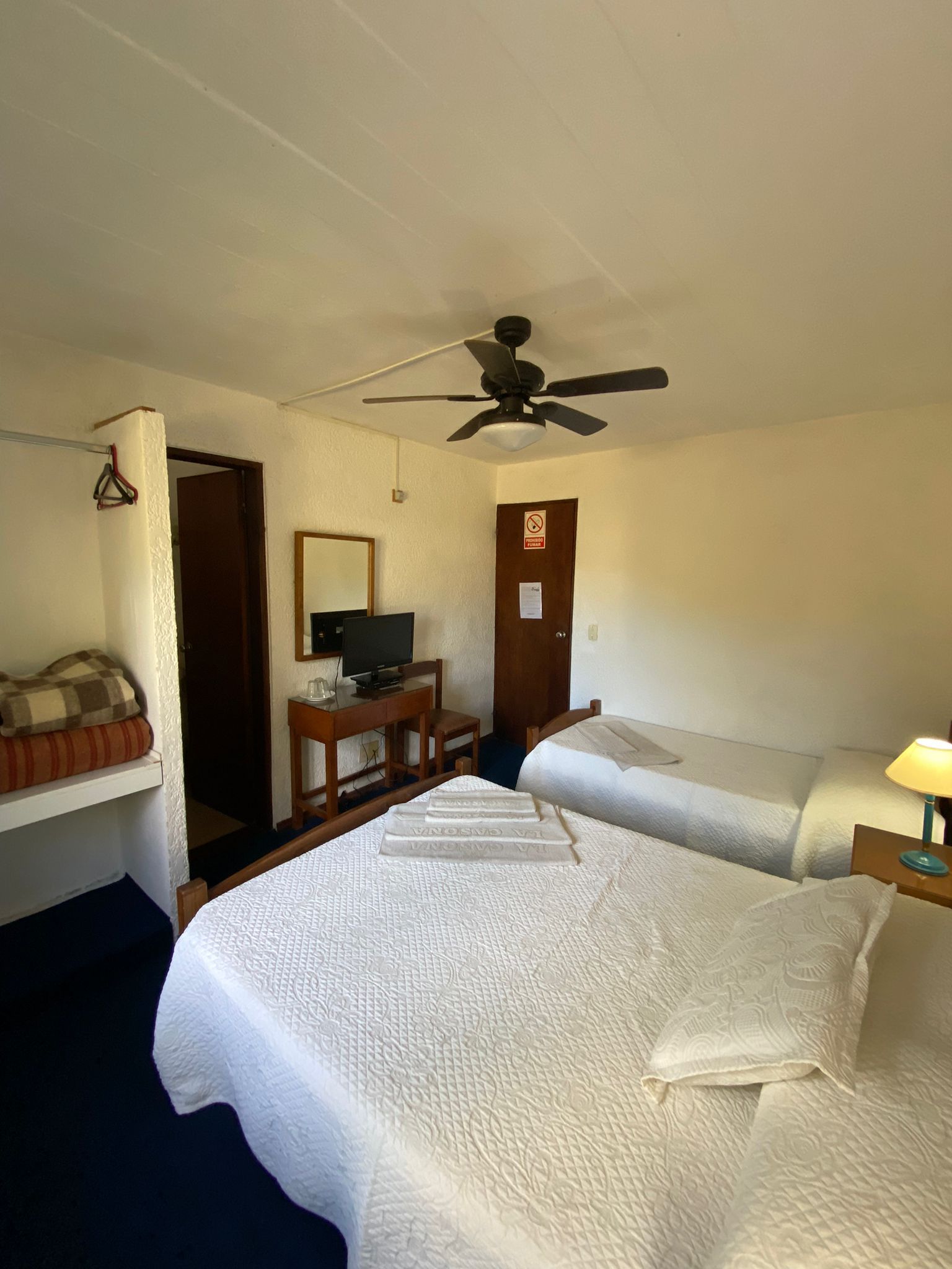 Habitación de hotel con dos camas, un televisor y un ventilador de techo.