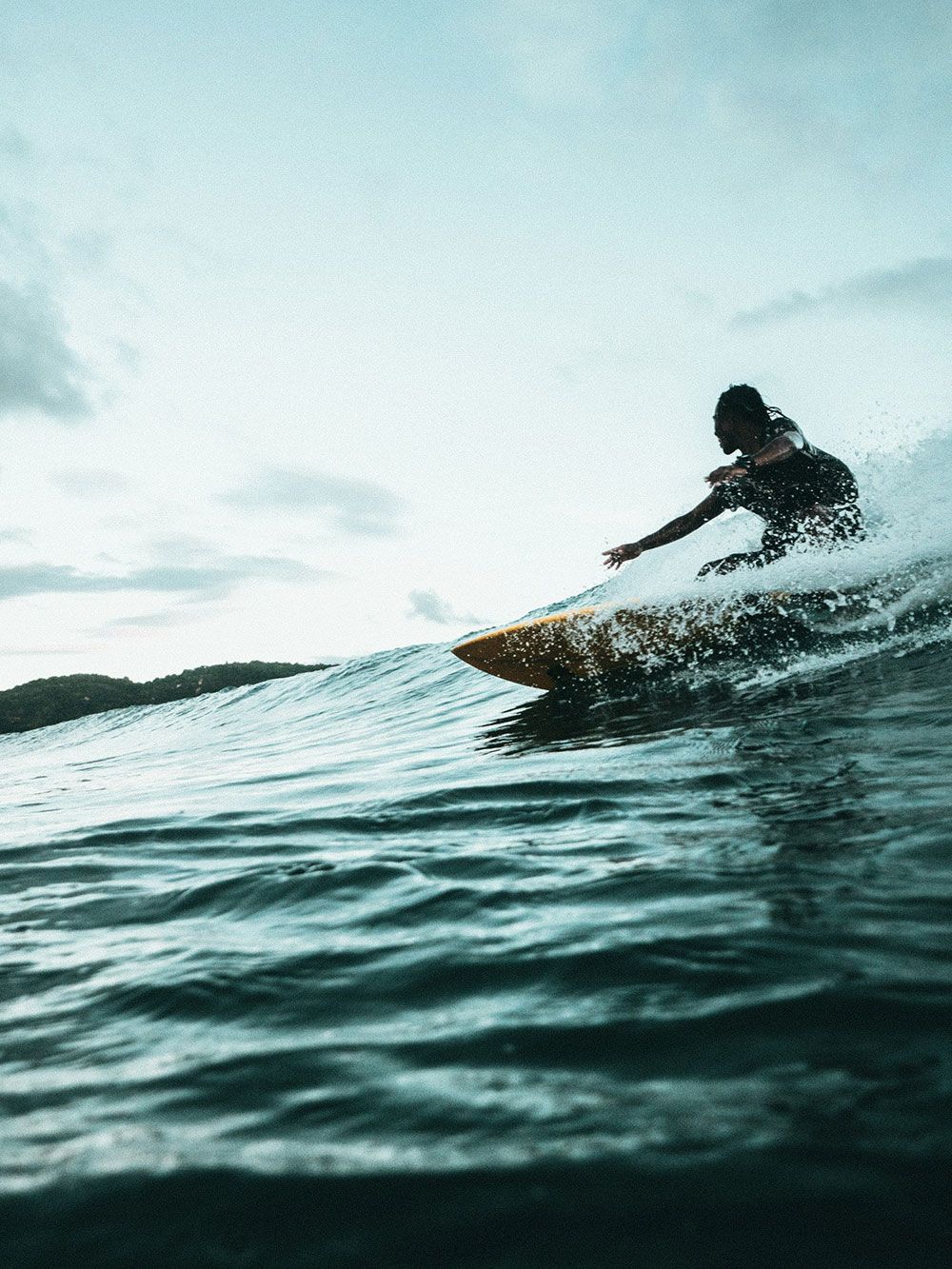 Surfista cabalgando una ola; escena oceánica. El surfista está de rodillas, con la mano extendida para mantener el equilibrio
