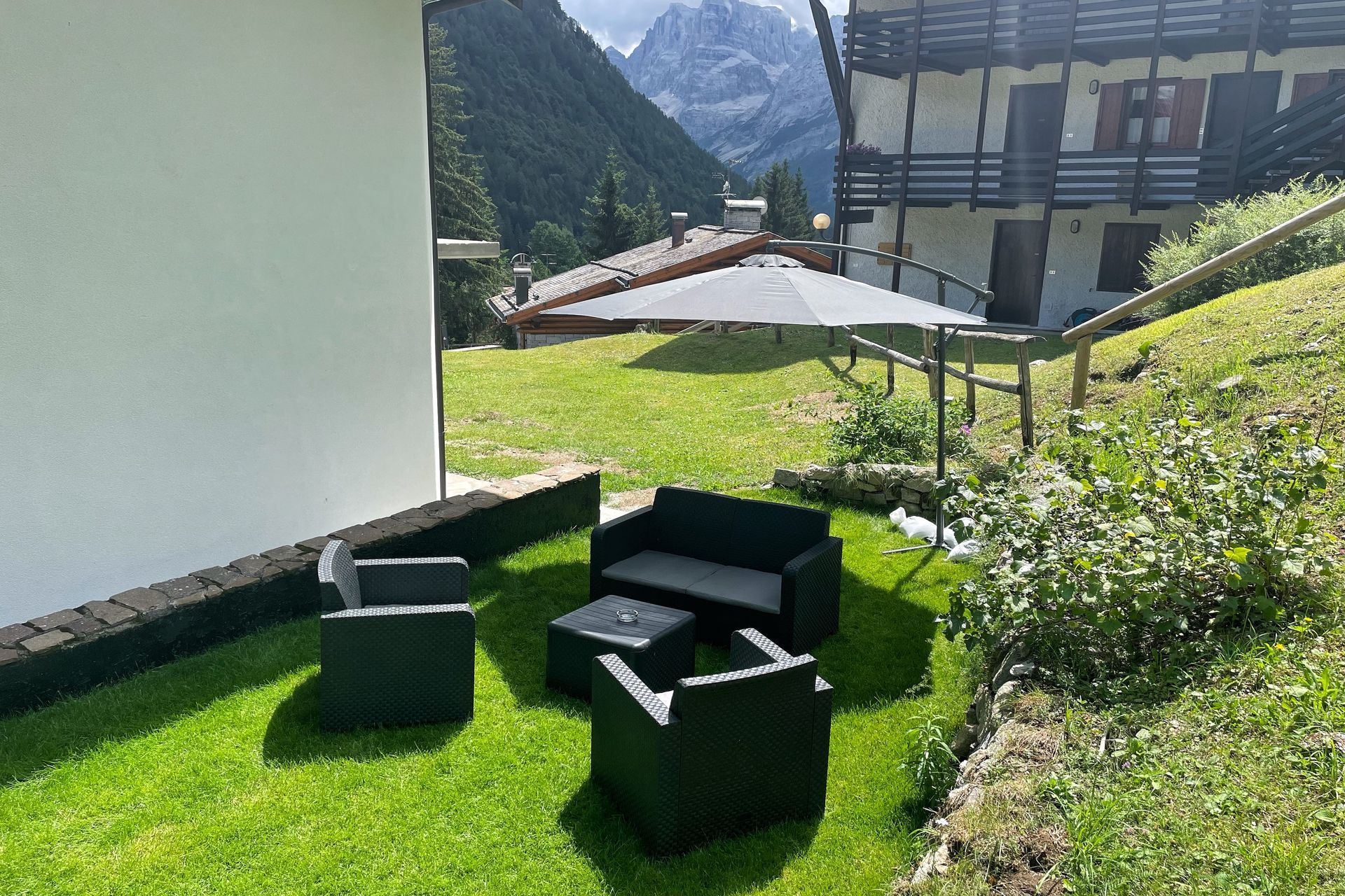 Un prato con un divano, sedie, tavolo e ombrellone davanti a una casa.