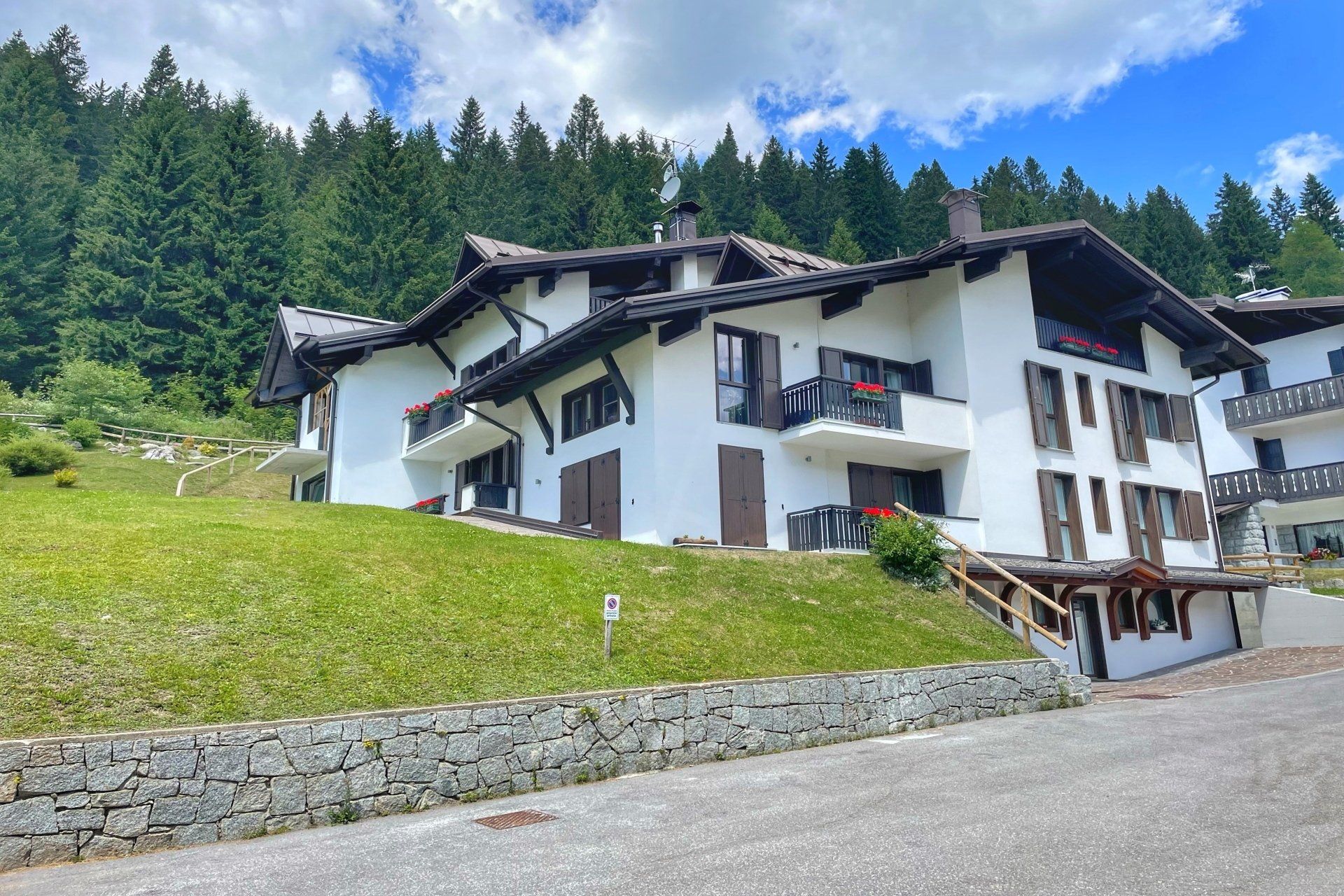 Una grande casa bianca si trova in cima a una collina erbosa circondata da alberi.