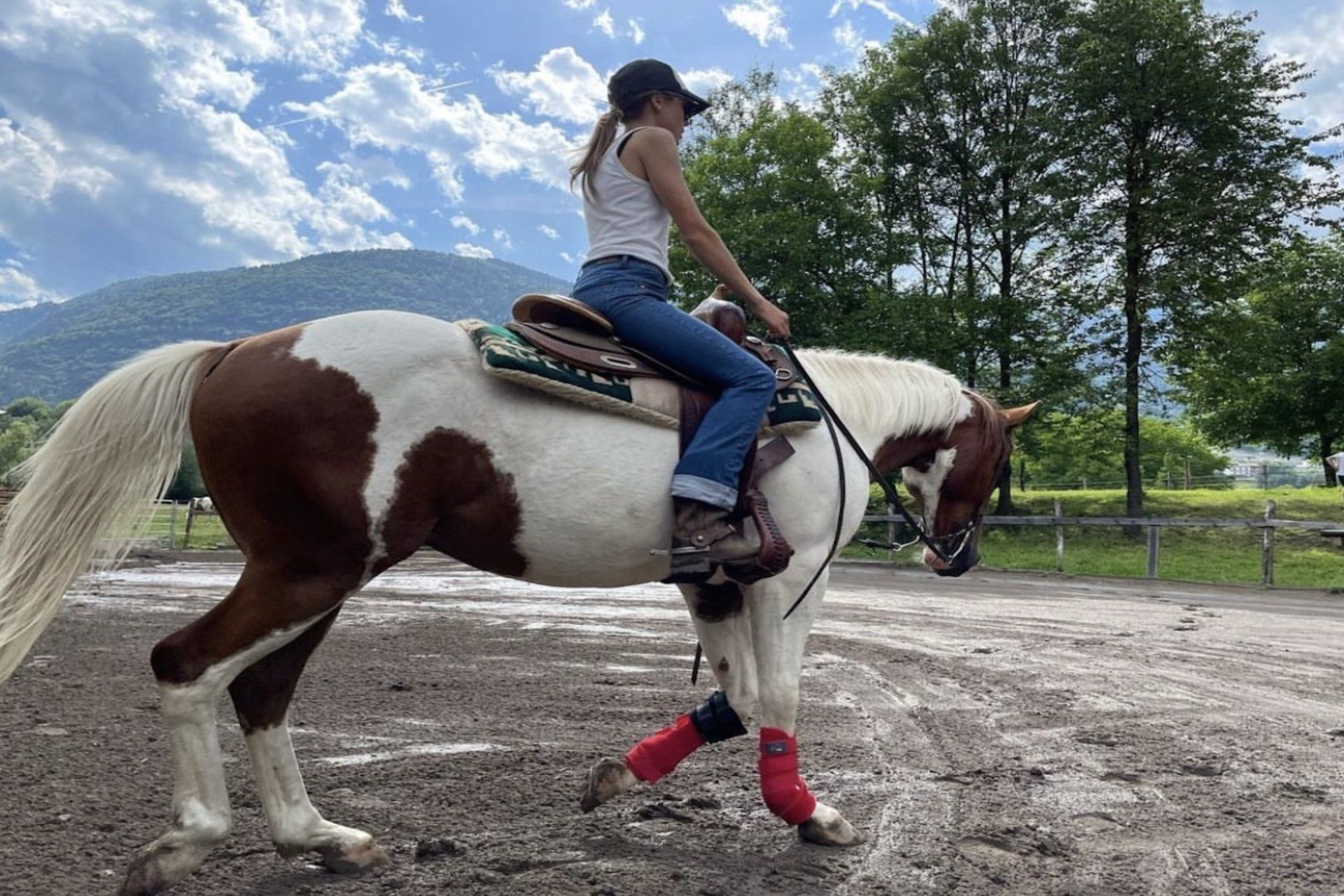 Una donna cavalca un cavallo marrone e bianco in un campo sterrato.