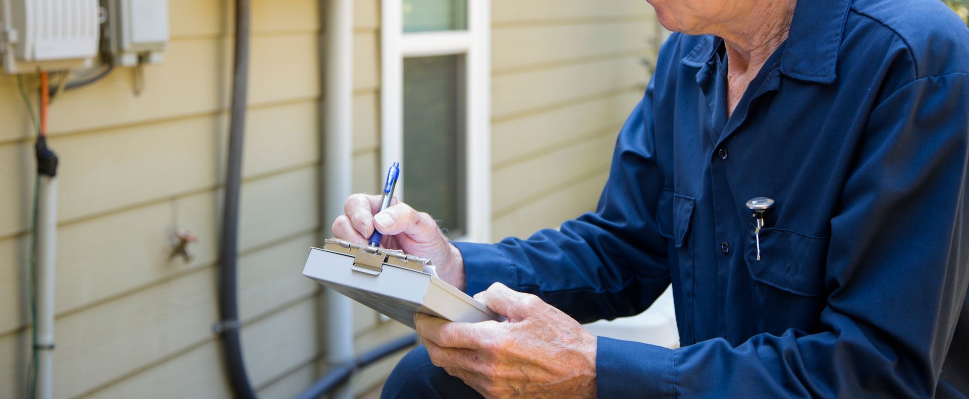 Person in blue shirt writing on a clipboard near a building's utility box.