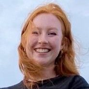 Smiling person with red hair, wearing a black shirt, outside.
