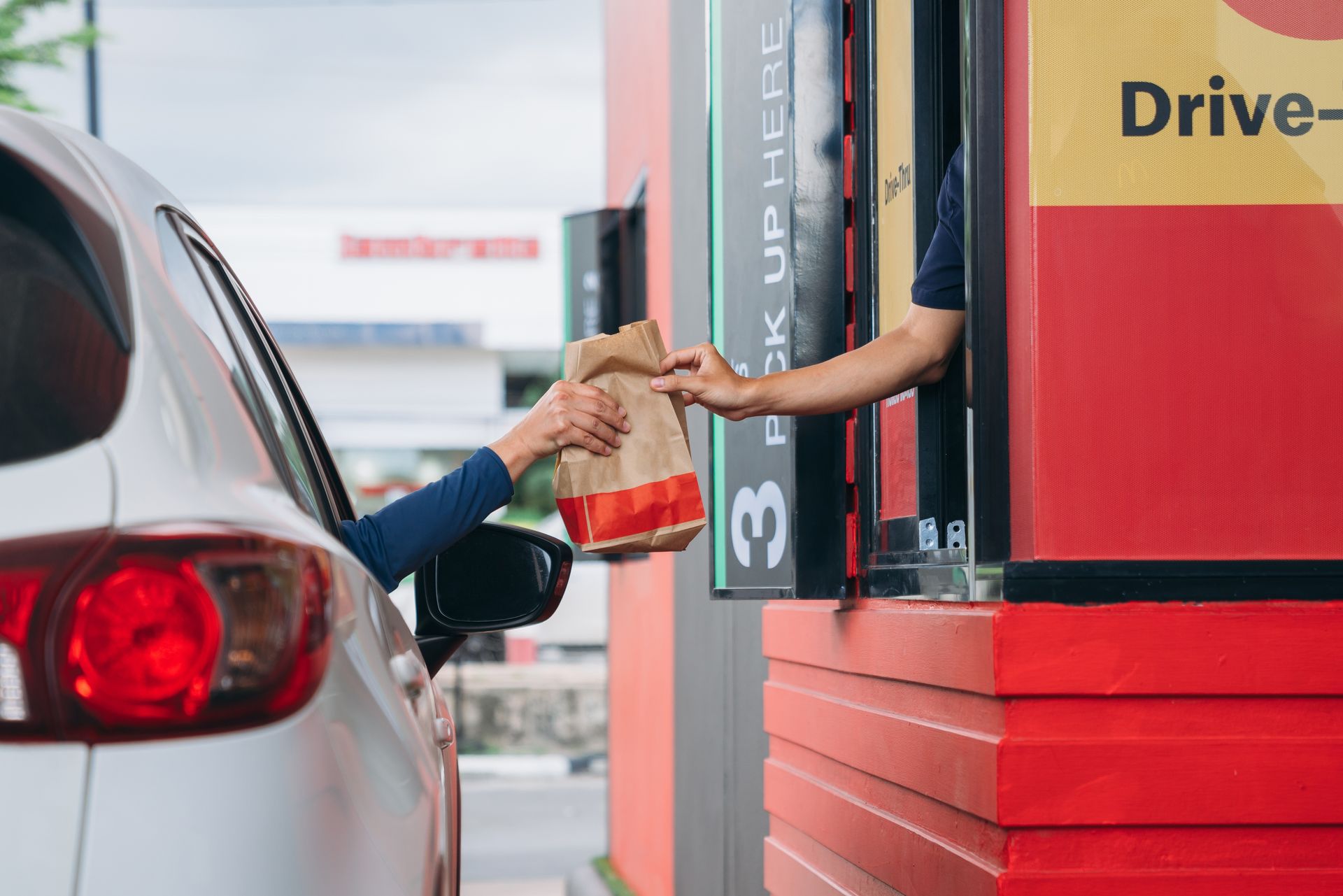 Handing a drink through a drive-thru window to a person in a car