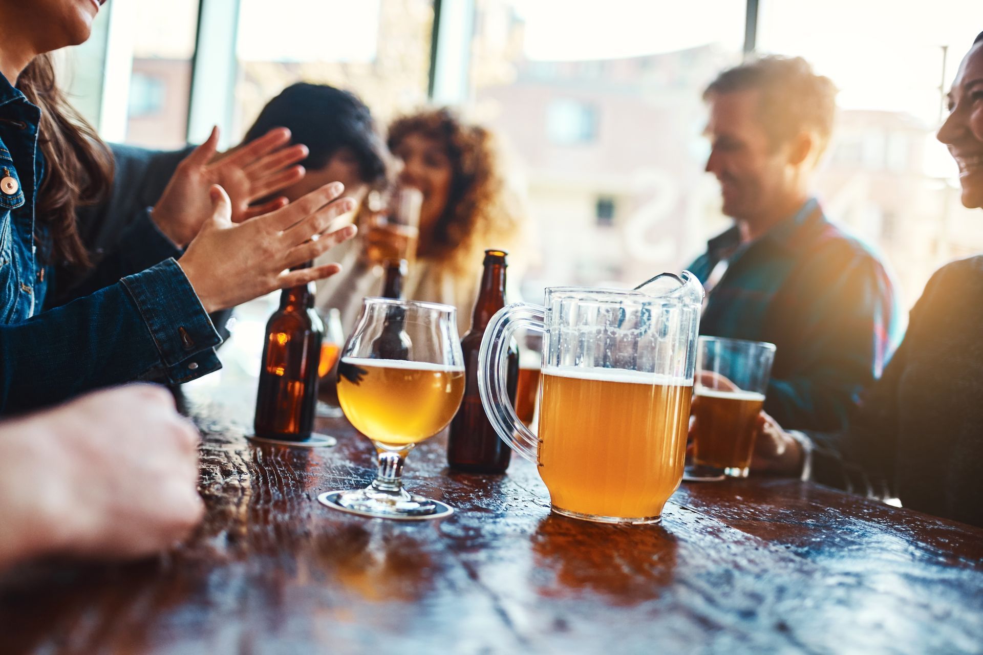 People clapping around beer glasses and a pitcher at a lively outdoor table