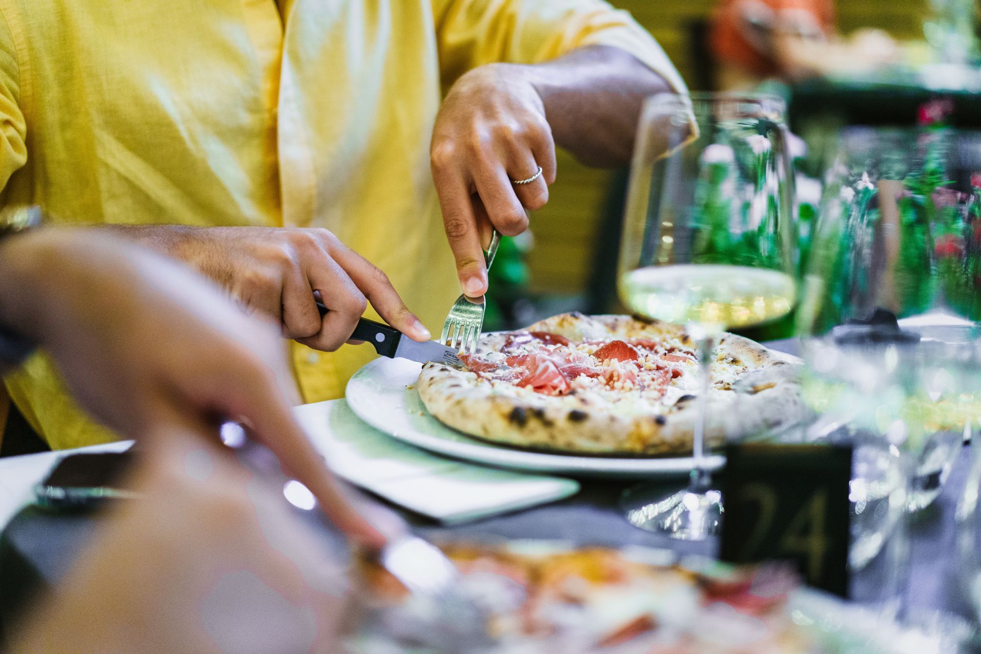 Hands serving pizza at a dinner table with green bottles and glasses