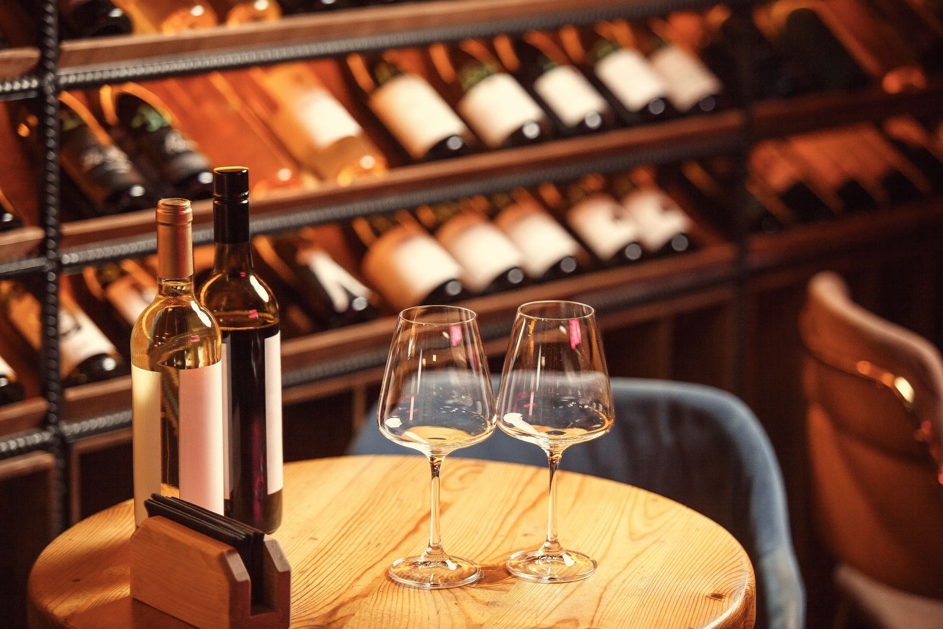 Wine bottles and two glasses on a wooden table in a warmly lit wine cellar