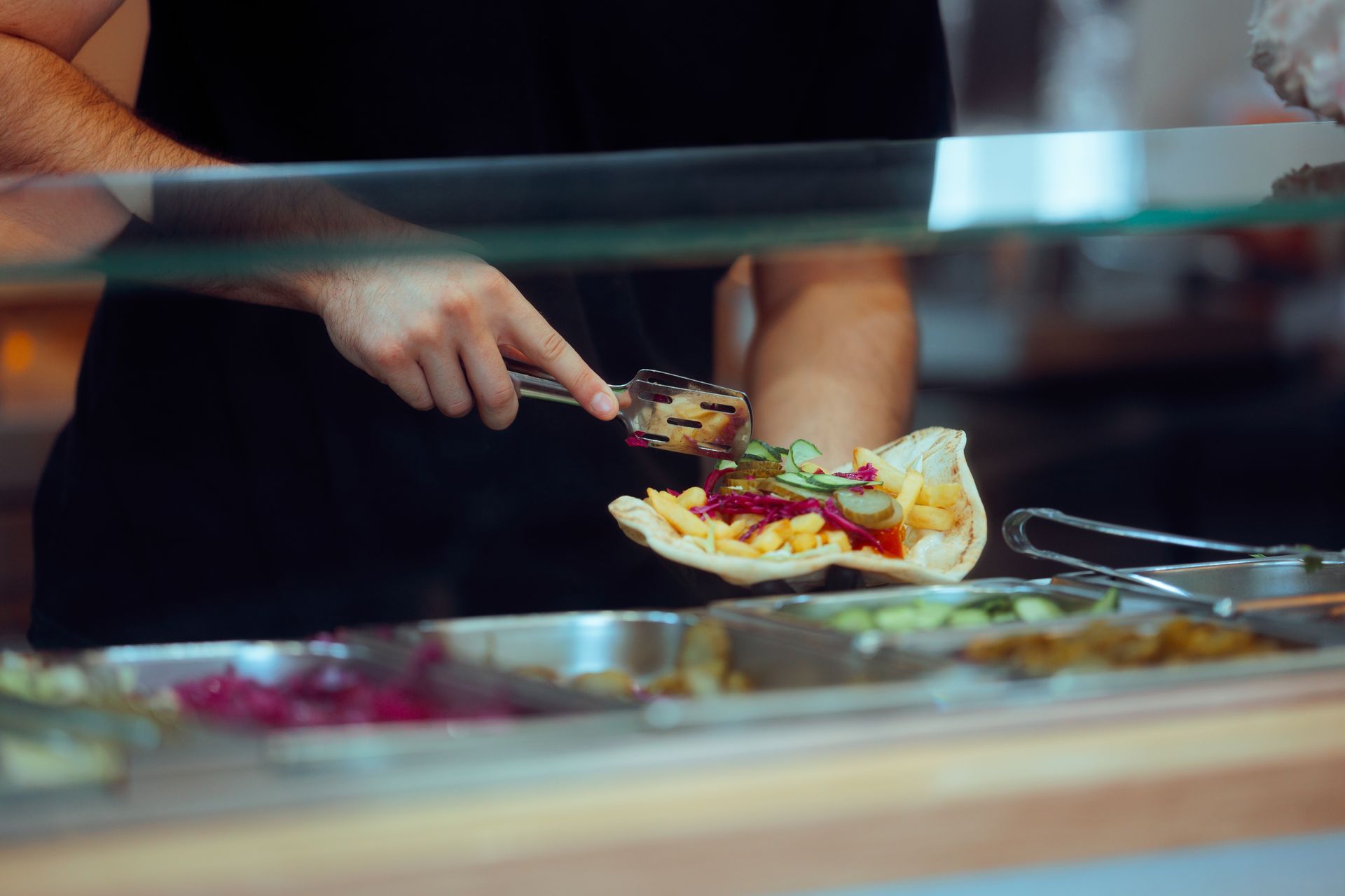 Person plating food at a buffet counter with tongs and a spoon