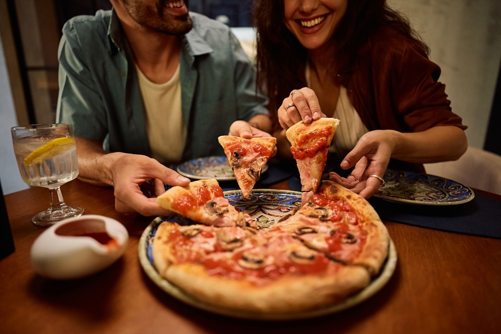 Two people sharing pizza at a table, lifting slices in a cozy restaurant setting