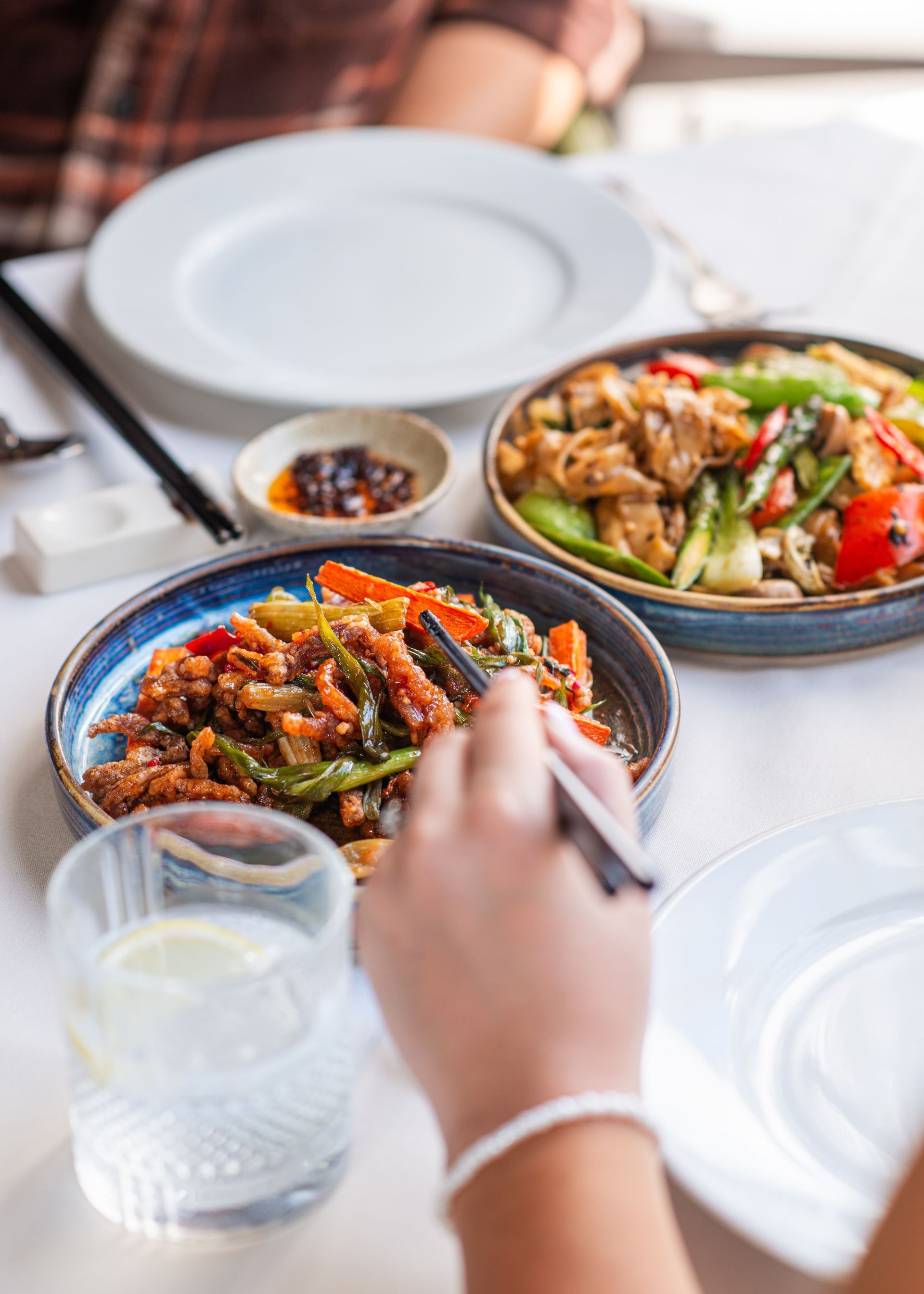Two bowls of colorful stir-fry on a dining table, with a hand reaching for one and empty plates nearby