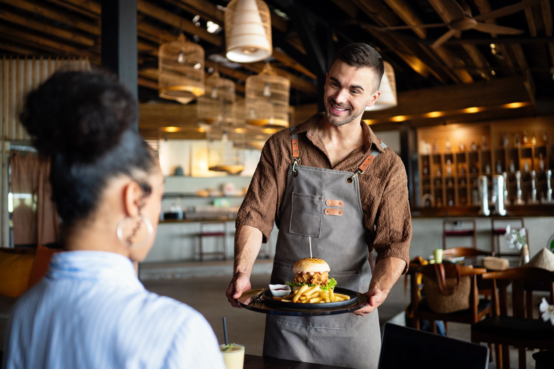 Waiter serving a burger on a tray to a seated customer in a warm-lit restaurant