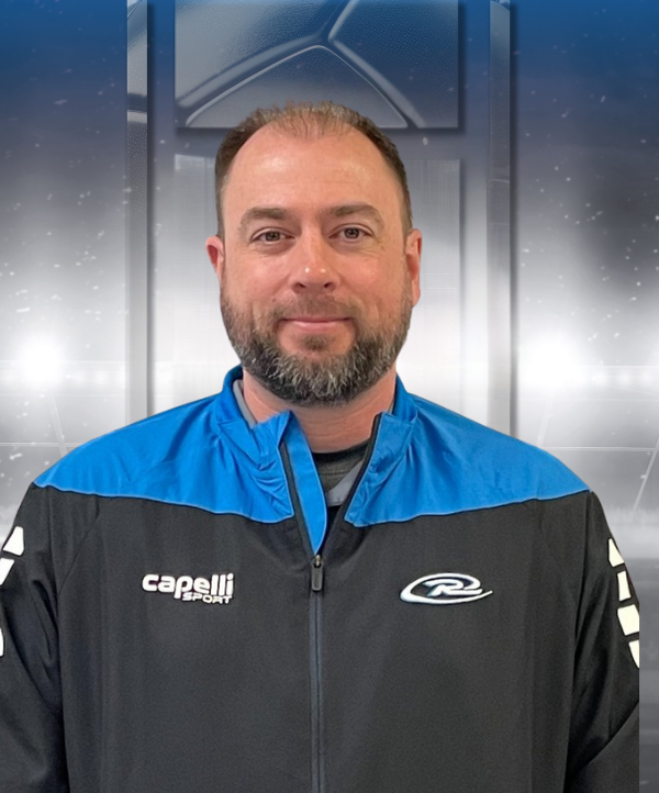 Man in a black and blue Capelli jacket standing before a metallic background, facing the camera with a slight smile