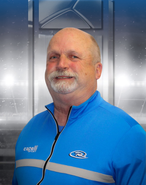 Smiling man in blue athletic jacket standing against a metallic gray background