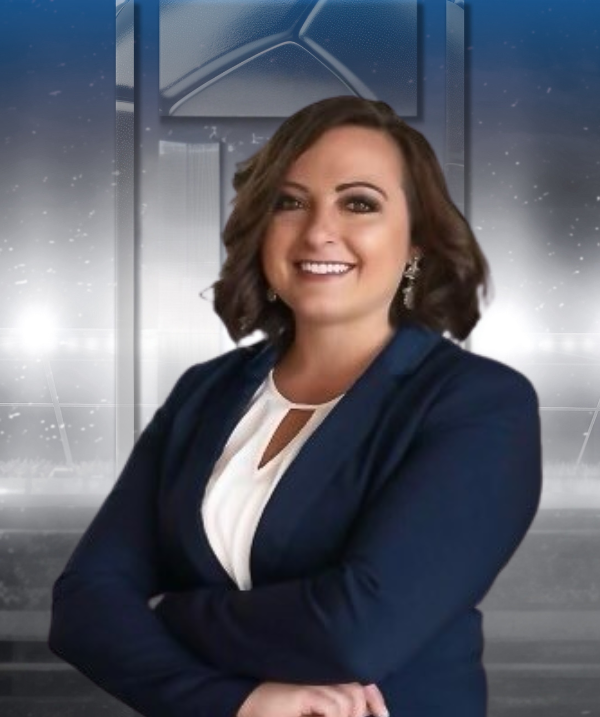 Smiling woman in a navy blazer and white blouse, posed with crossed arms against a gray studio backdrop