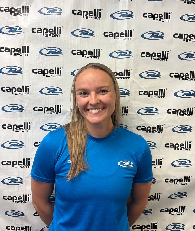 Smiling person in a blue shirt standing before a Capelli-branded backdrop.