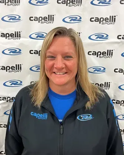 Smiling woman in a black Capelli jacket standing before a Capelli logo backdrop