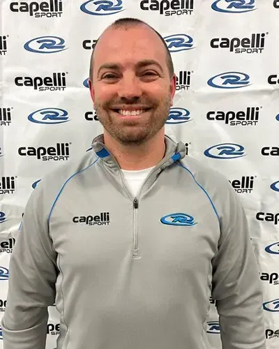 Smiling man in gray Capelli Sport jacket posing in front of a Capelli Sport logo backdrop