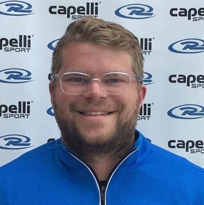 Smiling man in glasses wearing a blue jacket in front of a Capelli Sport backdrop