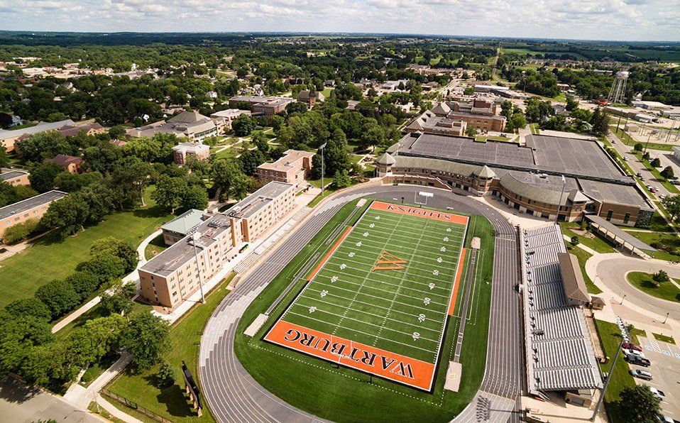 Aerial view of a football stadium with an orange field and surrounding campus buildings.