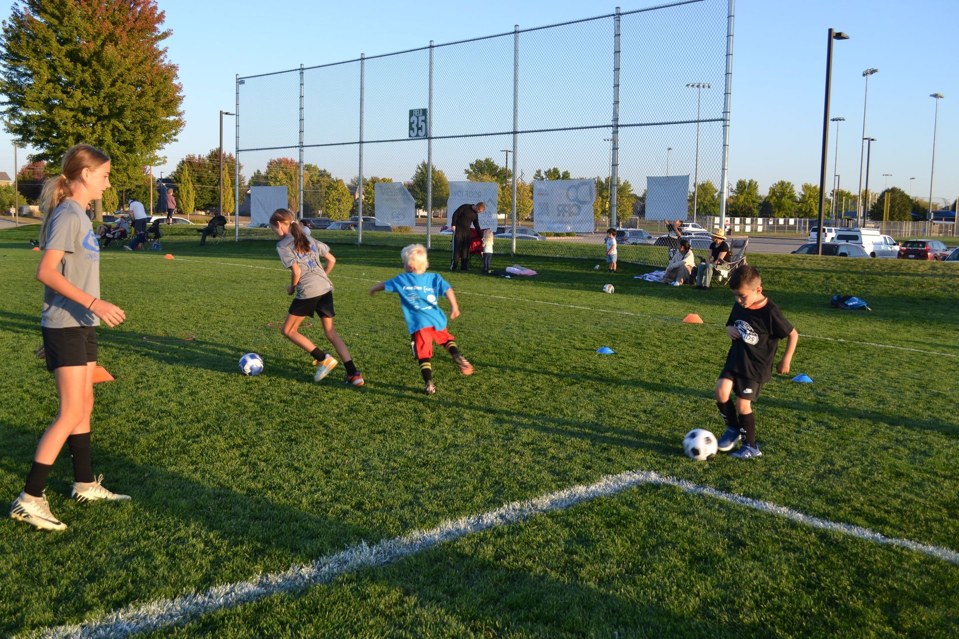 Children practicing soccer drills on a sunny outdoor field with cones and goals in the background