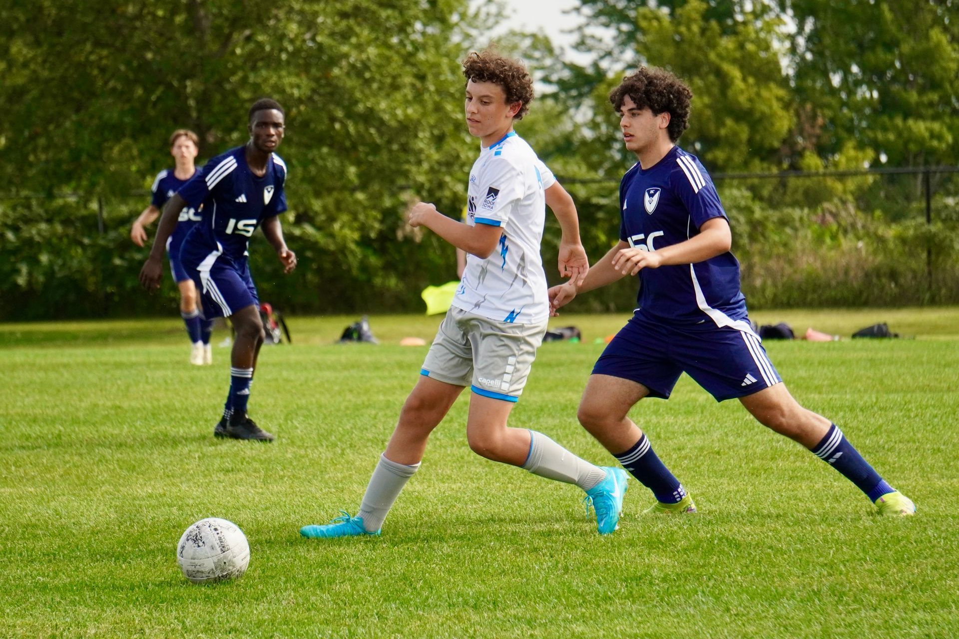 Soccer players in blue and white jerseys chase the ball on a grassy field.