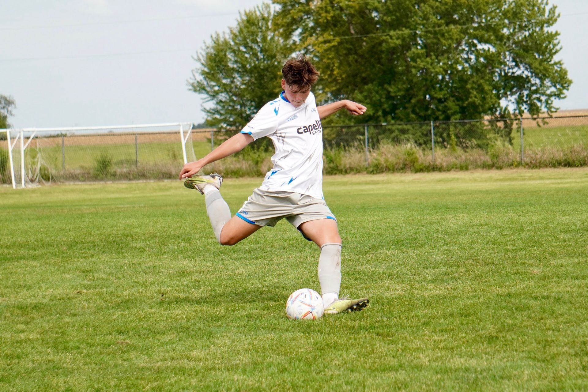 Soccer player in white kicking a ball on a grassy field