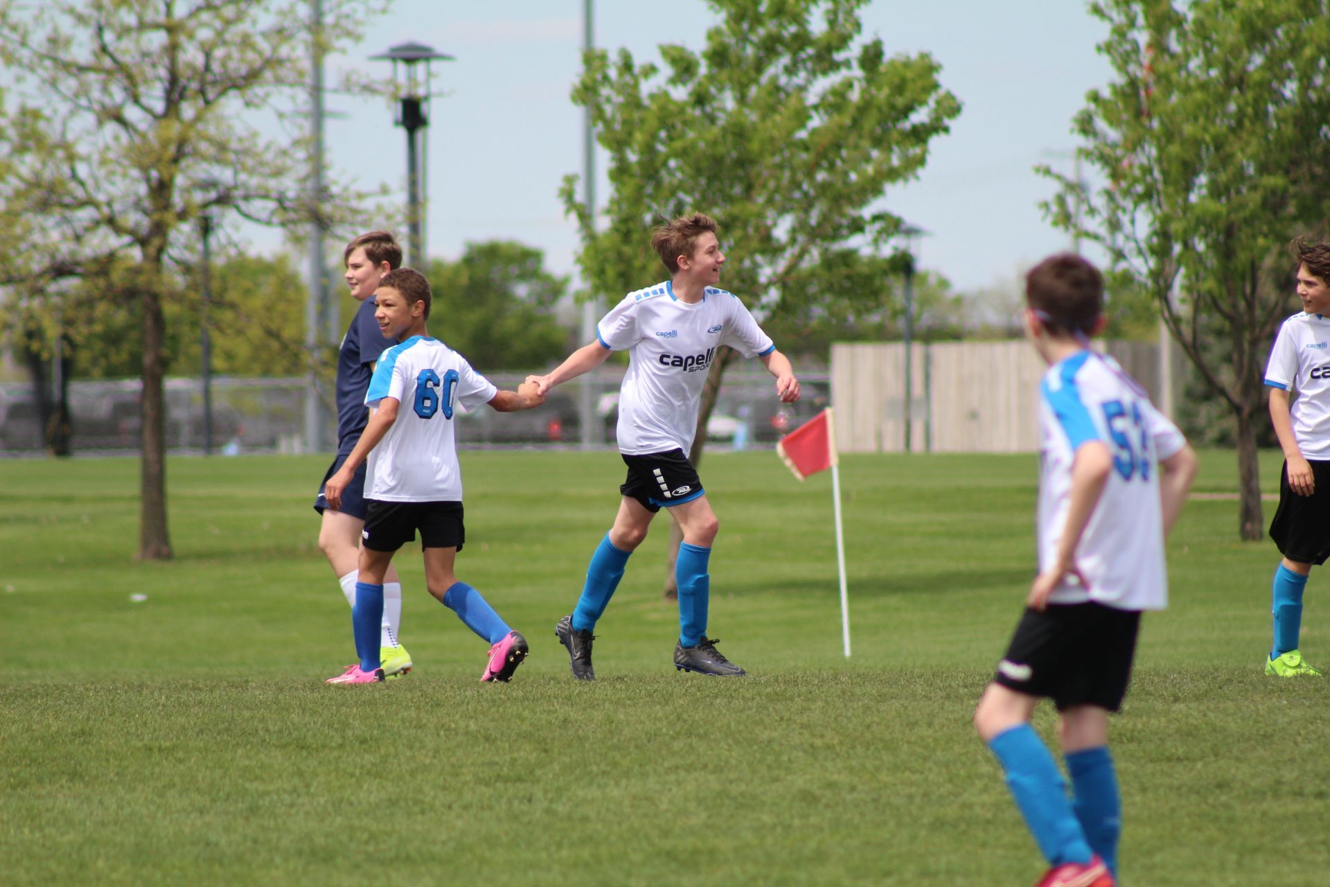 Soccer players on a grassy field near a corner flag, with one player holding a pink flag