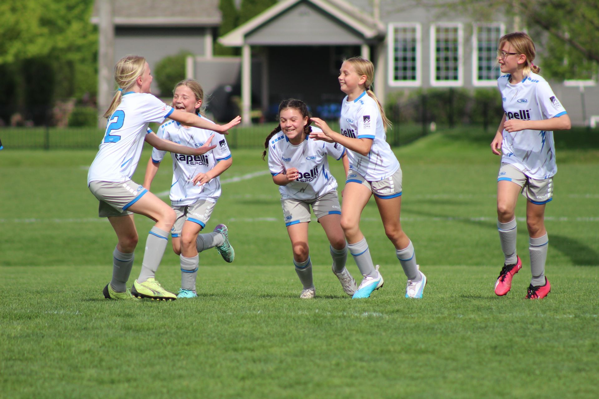 Children in white sports uniforms playing on a grassy field outdoors