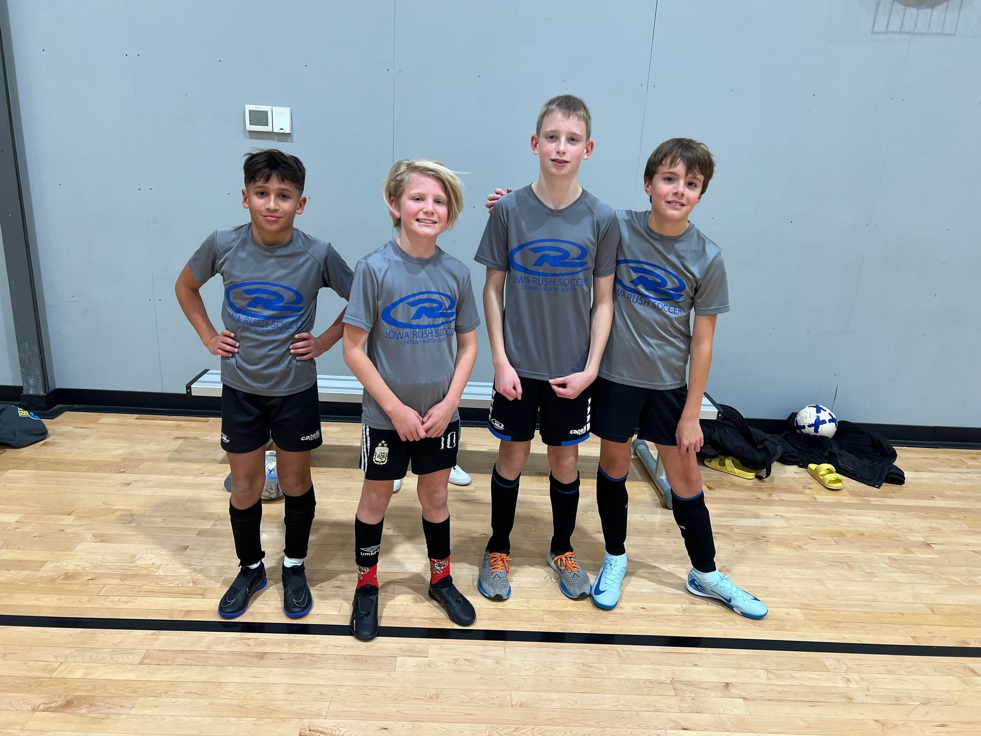 Four youth volleyball players in gray jerseys posing indoors on a gym floor.