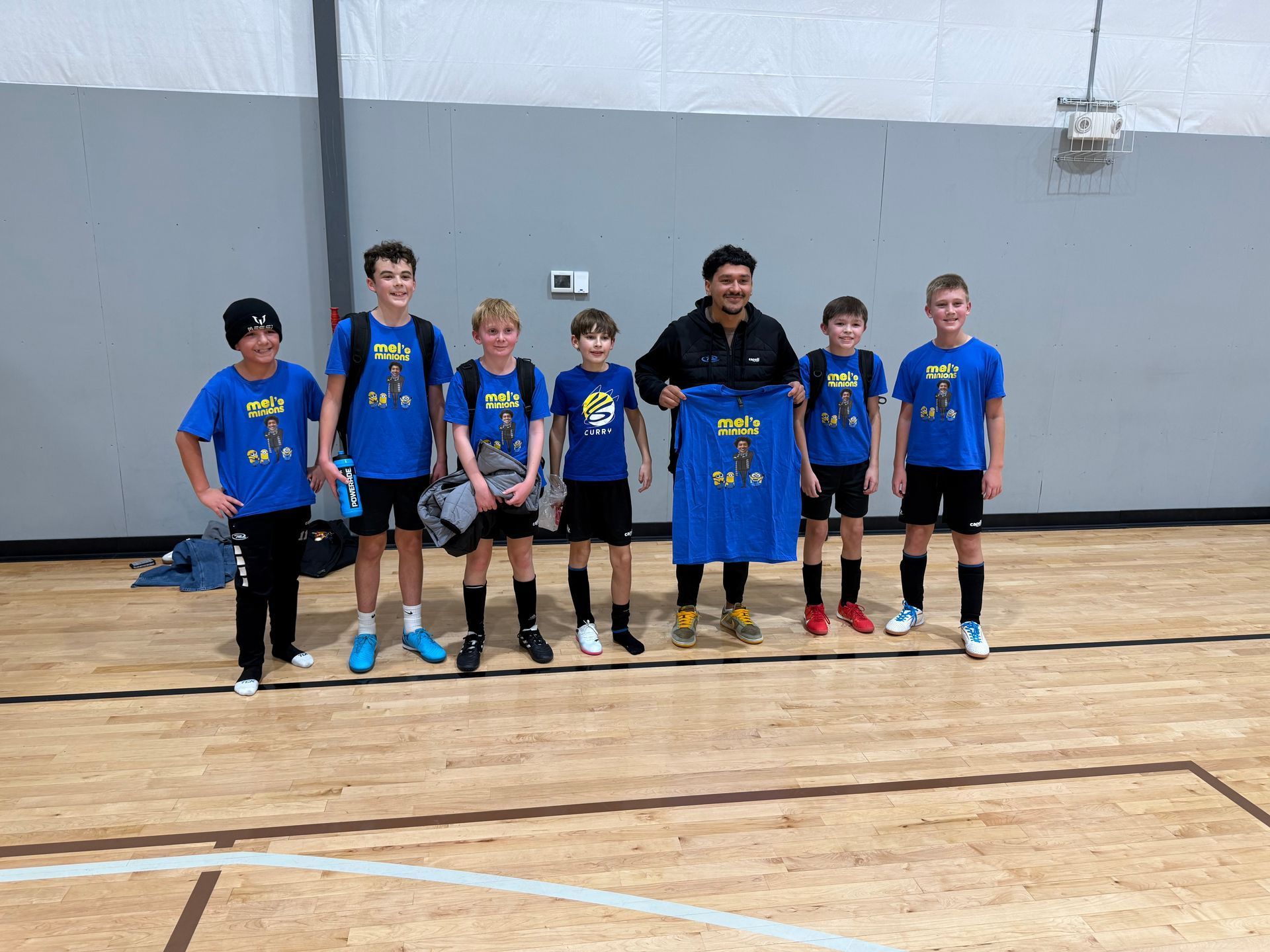 Seven youths in blue jerseys pose on an indoor basketball court, holding a blue banner.