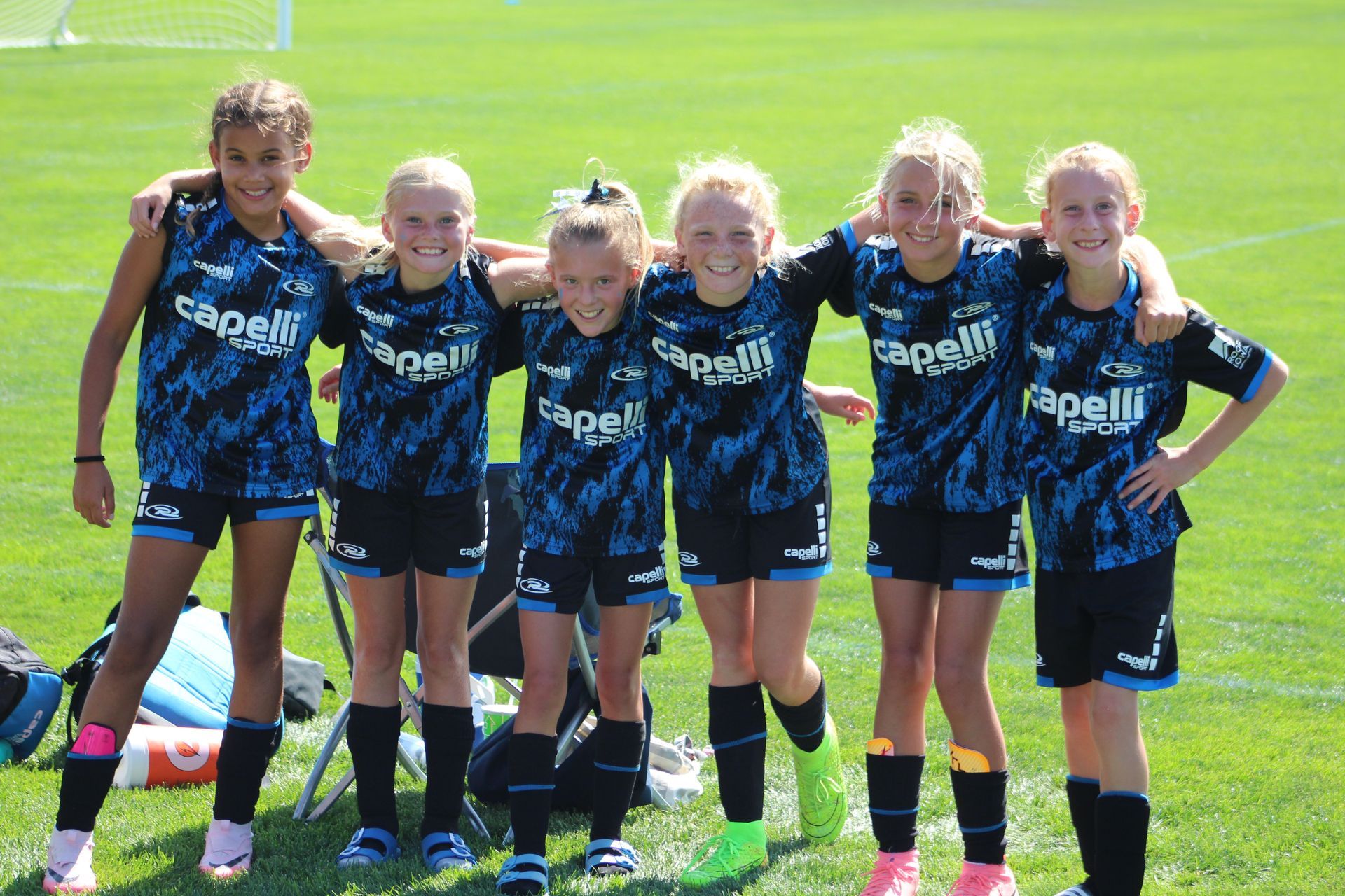 Six youth soccer players in dark blue uniforms standing together on a grass field