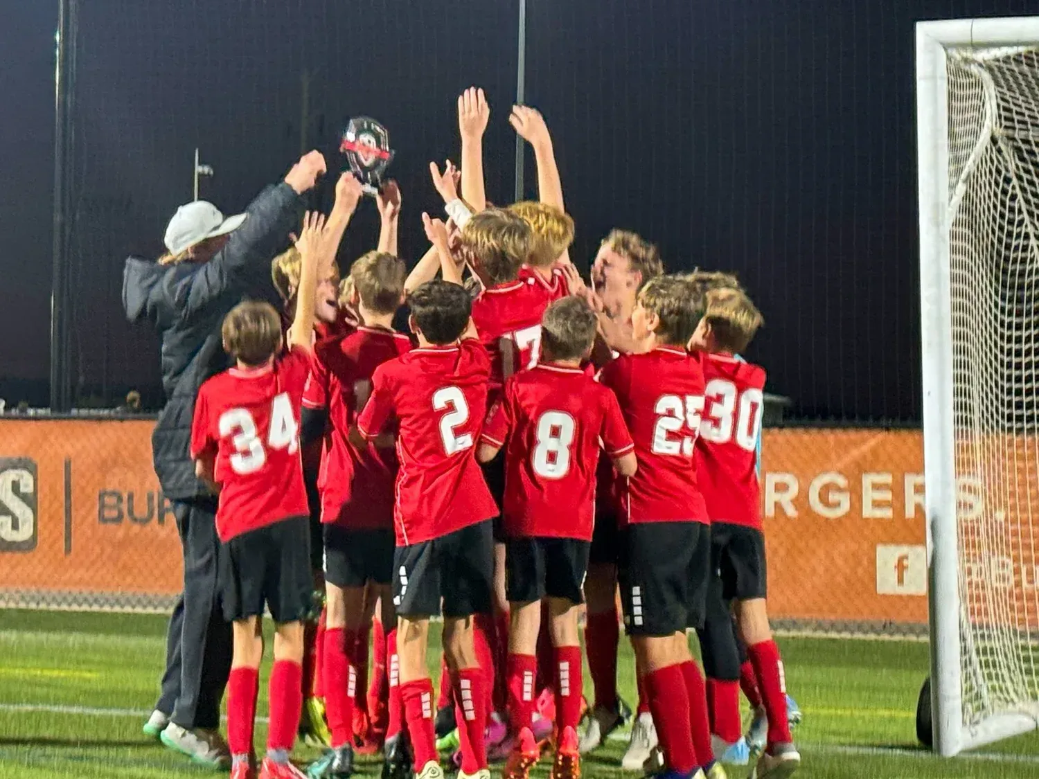 Soccer players in red jerseys huddle and cheer beside the goal after a match-winning moment.