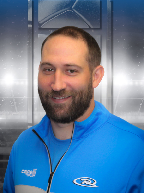 Smiling man in a blue zip-up jacket standing indoors against a metallic background