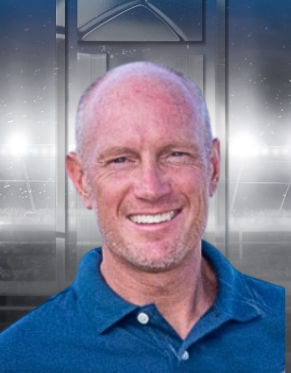 Smiling bald man in a blue polo shirt against a blurred metallic background