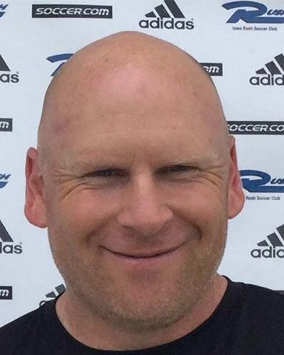 Smiling bald man in a black shirt in front of a Soccer.com and adidas backdrop