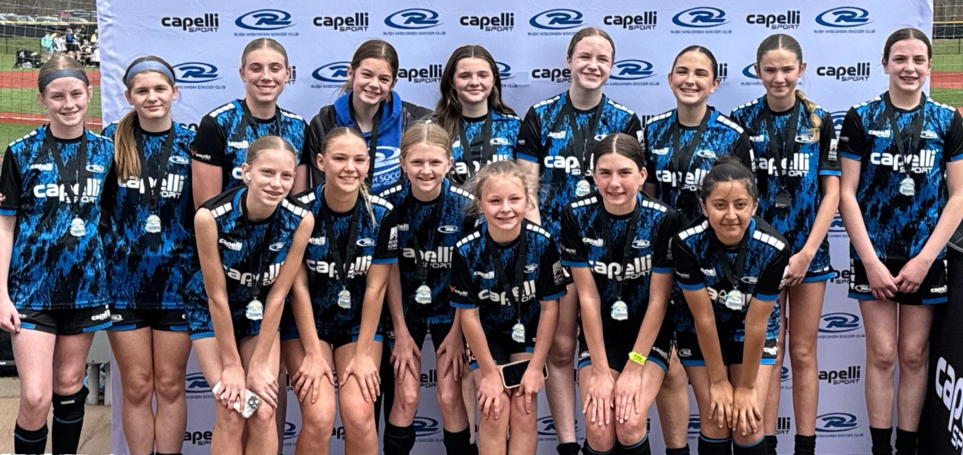 Group of young athletes in matching blue-and-black uniforms posing for a team photo in front of sponsor logos