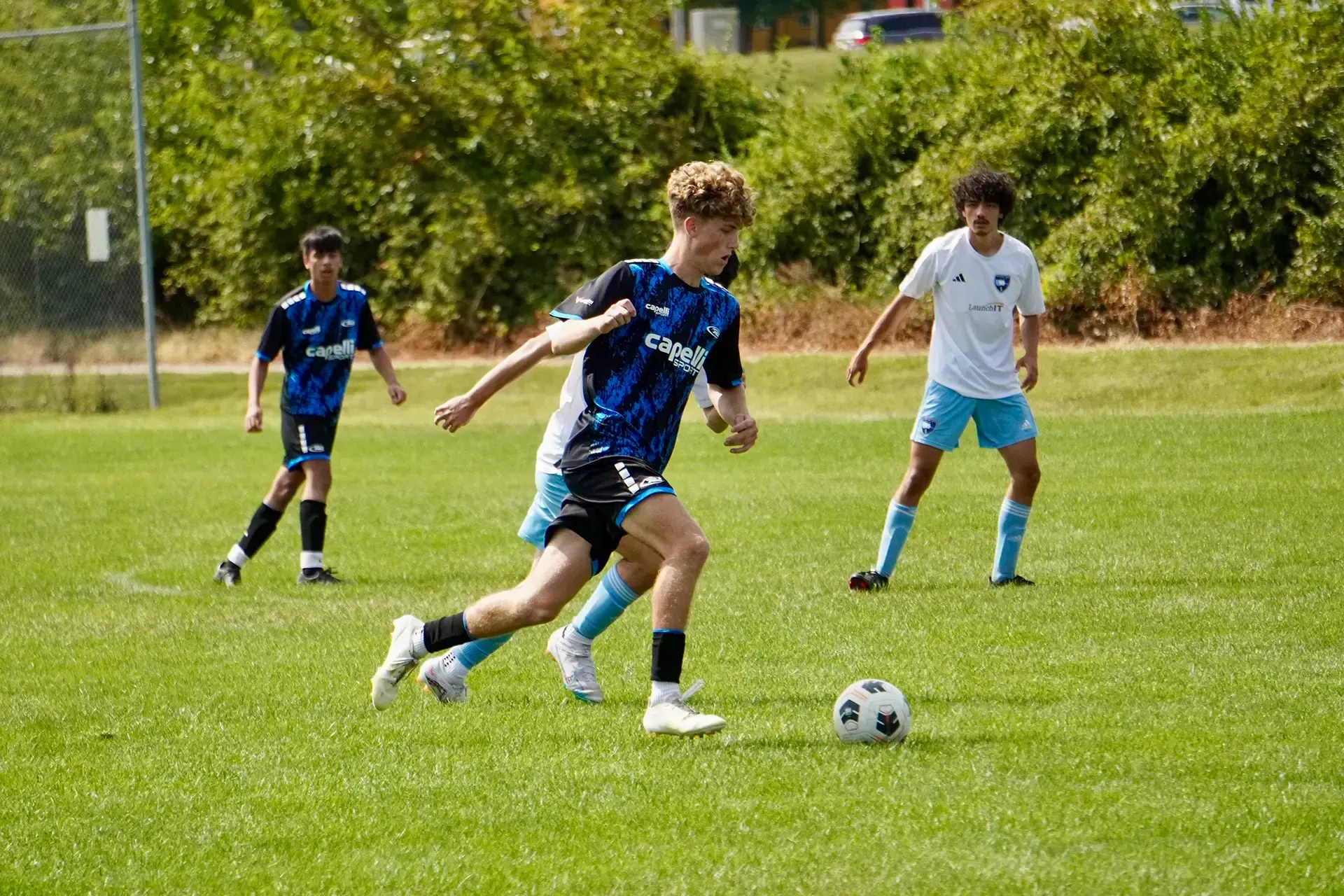 Soccer player in blue dribbles on a grassy field while two players defend nearby.