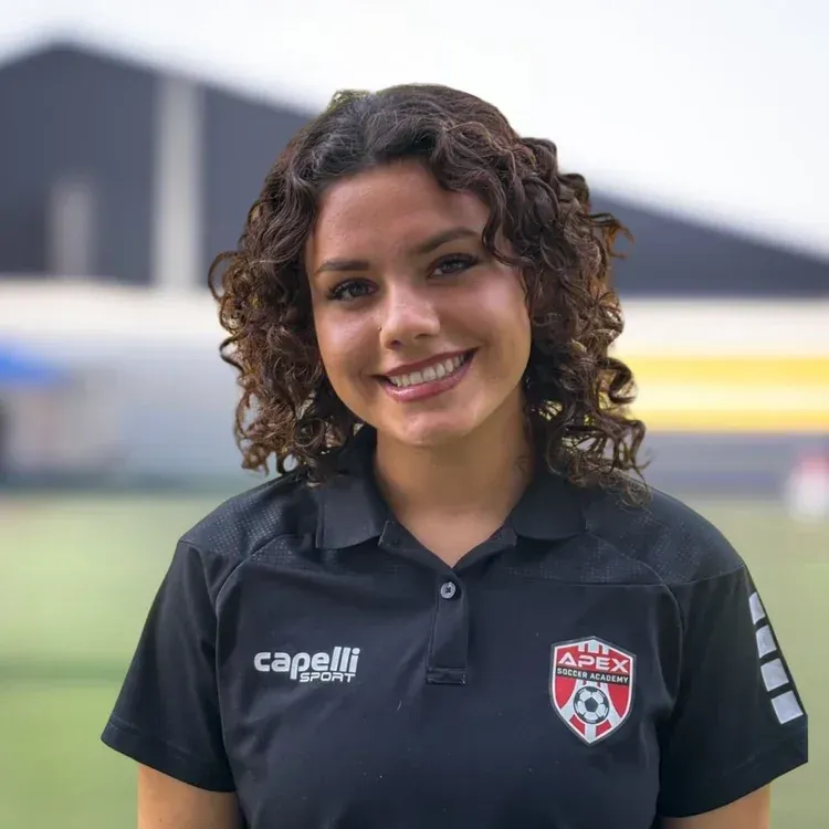 Smiling athlete in black Capelli polo with team crest, standing outdoors on a field