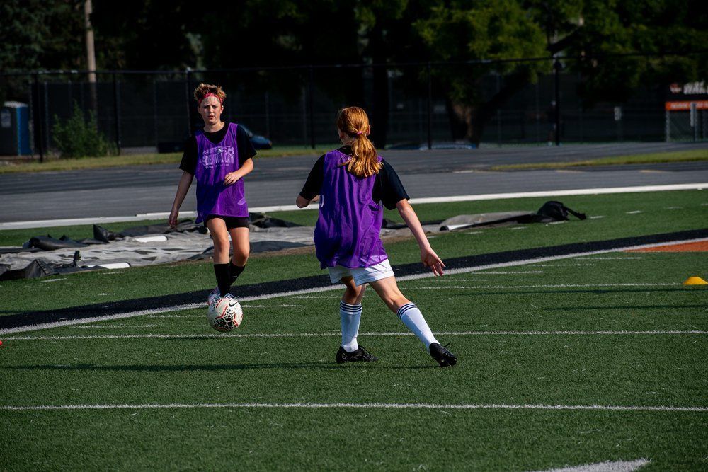 Two players in purple jerseys pass a soccer ball on a green field.