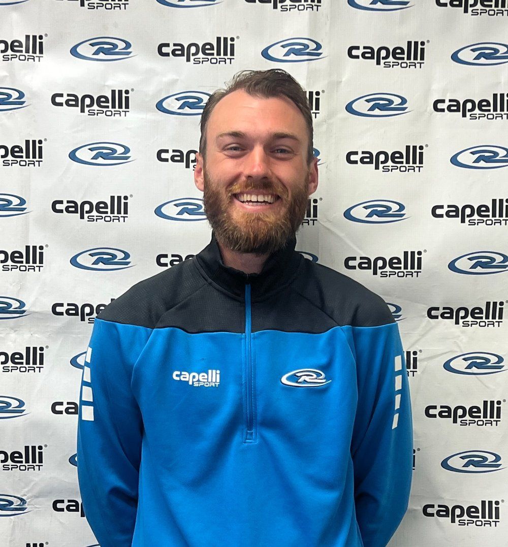 Smiling man in a blue Capelli jacket standing before a Capelli logo backdrop