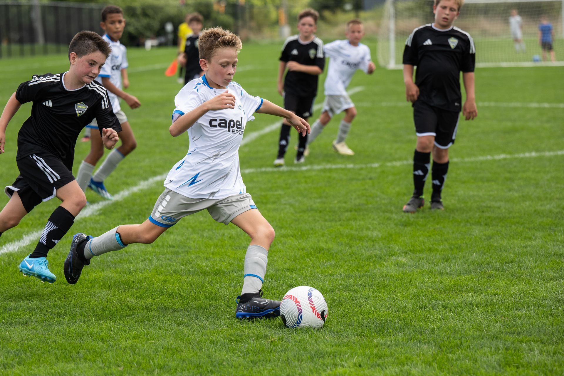 Youth soccer game with players sprinting on a grassy field, one in white dribbling the ball