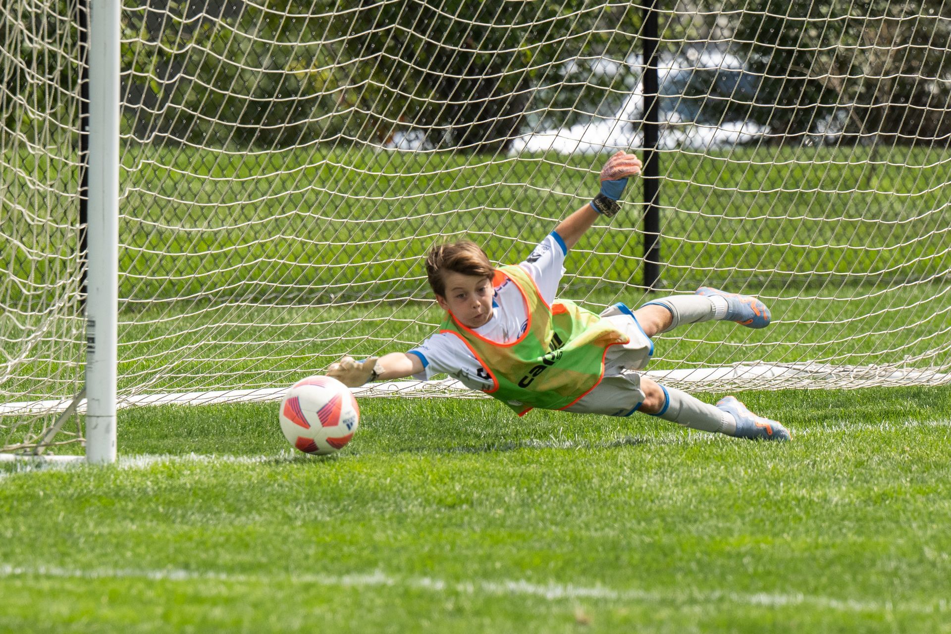 Soccer goalkeeper diving on grass to block a ball in front of the goal