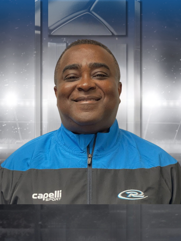 Smiling man in a blue and gray jacket against a blurred metallic backdrop